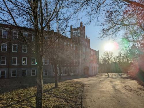Sunlight shines on a historic brick building surrounded by bare trees and a winding path.