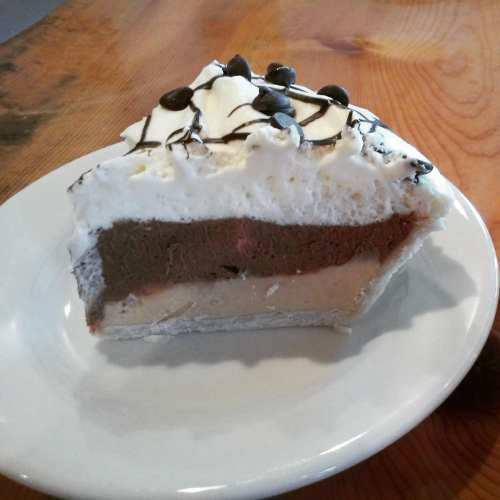 A slice of layered chocolate cream pie topped with whipped cream and chocolate chips on a white plate.