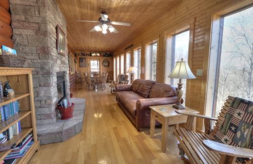 Cozy wooden interior with a stone fireplace, leather sofa, and large windows overlooking a natural landscape.