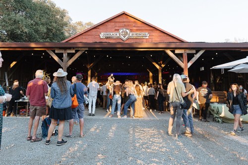 A crowd gathers outside a rustic barn venue during an event, with people mingling and enjoying the atmosphere.