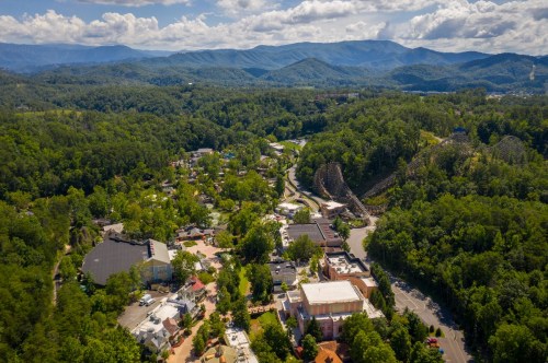 Aerial view of a lush green valley with mountains, featuring a small town and amusement park rides in the distance.