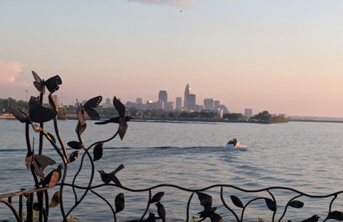 A scenic view of a city skyline at sunset, with a decorative metal railing and a boat on the water in the foreground.
