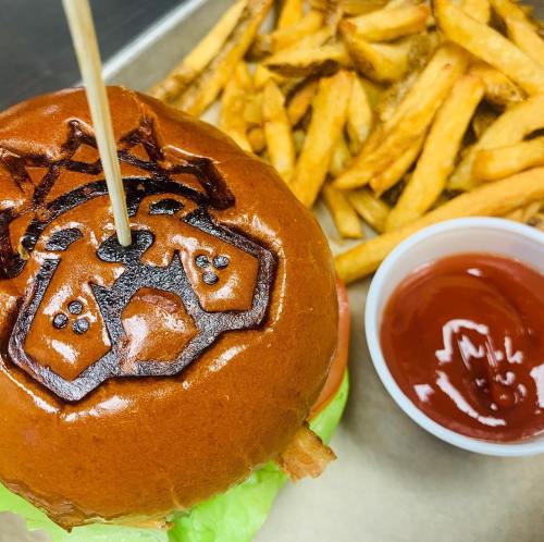 A burger with a logo on the bun, served with fries and a side of ketchup.