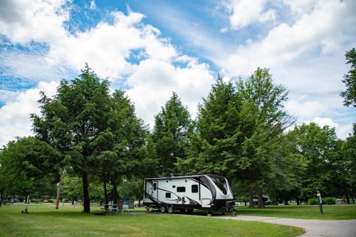 A camper parked in a green park surrounded by trees under a partly cloudy sky.