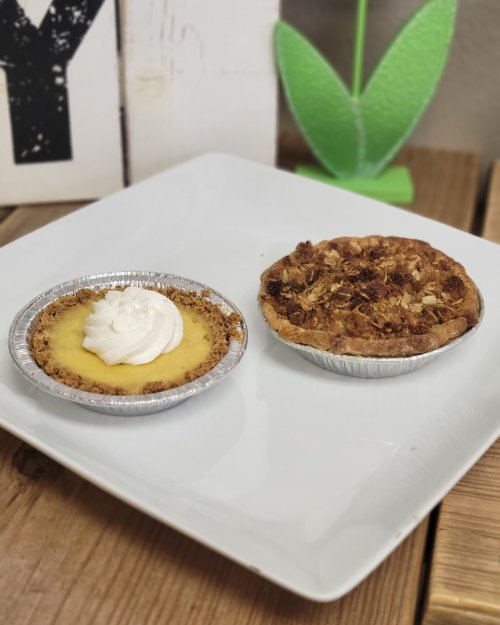 Two mini pies on a white plate: one with a creamy filling and whipped cream, the other topped with a crumbly oat mixture.