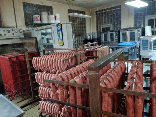 A meat processing room with racks of sausages hanging and various kitchen equipment in the background.