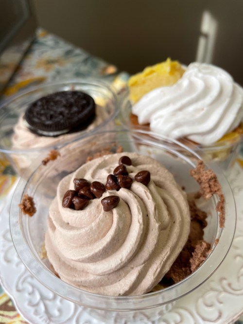Three dessert cups featuring chocolate mousse topped with coffee beans, an Oreo, and a yellow cream swirl.