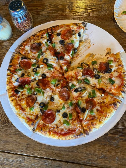 A pizza topped with pepperoni, olives, green peppers, and cheese, partially sliced on a round cardboard base.