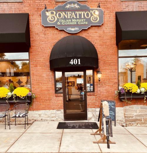 Entrance of Bonfatto's Italian Market & Corner Café, featuring a brick facade, awning, and colorful flower planters.