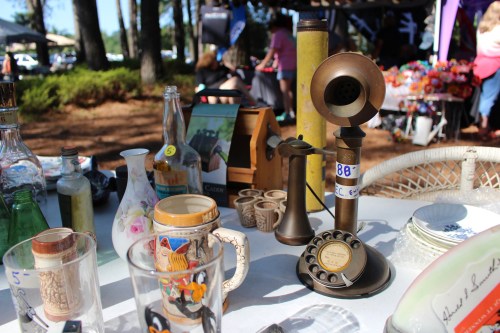 A table filled with vintage items, including a rotary phone, glassware, and decorative bottles at an outdoor market.