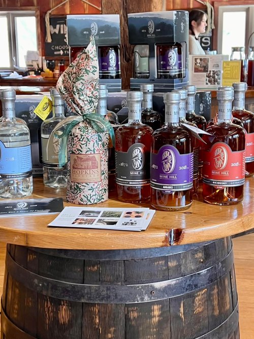 A wooden barrel displays various bottles of spirits, with a decorative gift bottle in the foreground and brochures nearby.