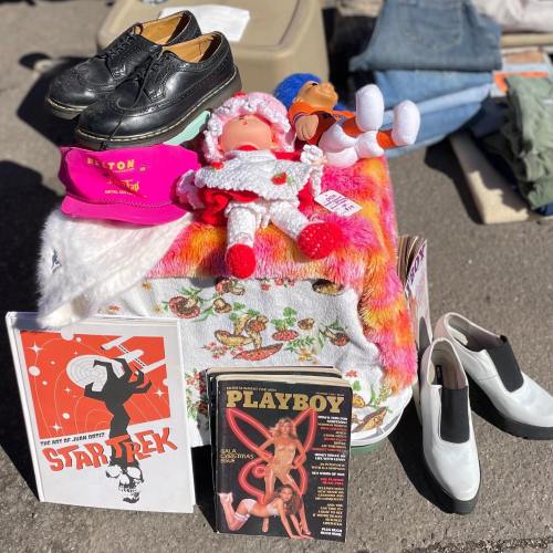 A colorful display of shoes, dolls, and vintage magazines on a table at a flea market.