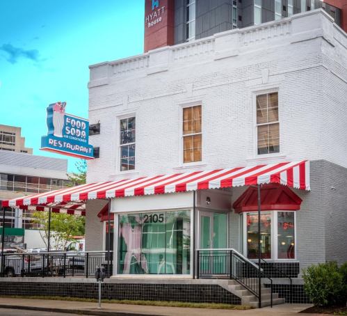A vintage-style restaurant with a red and white striped awning and a neon sign, located in a city setting.