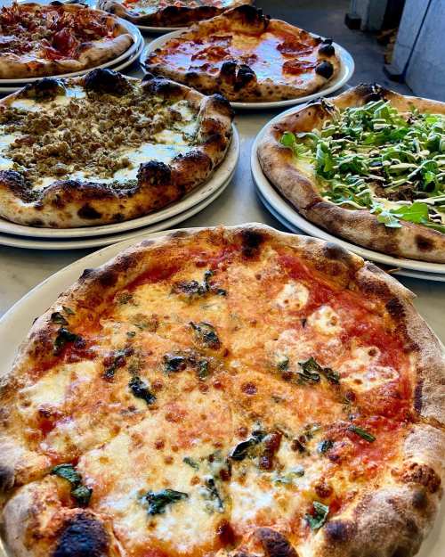 A variety of pizzas on plates, including cheese, pepperoni, and veggie toppings, displayed on a table.