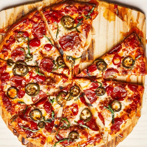 A freshly baked pizza topped with pepperoni, jalapeños, and melted cheese, sliced into eight pieces on a wooden board.