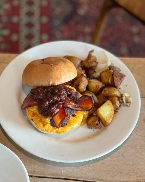 A plate featuring a burger with cheese and barbecue sauce, accompanied by roasted potatoes.