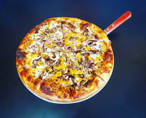 A delicious pizza topped with cheese, pulled meat, onions, and a golden crust, served on a metal pizza tray.