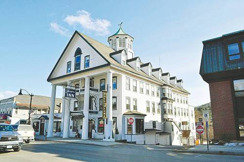 Historic white inn with a large porch and a cupola, set against a clear blue sky.
