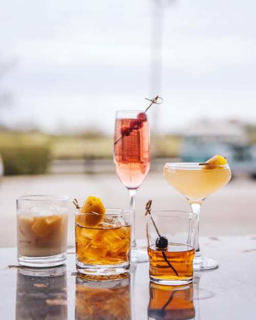 A variety of colorful cocktails in different glasses, featuring garnishes like cherries and citrus, on a table.