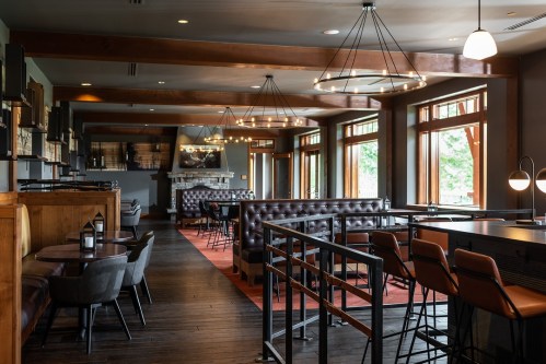 A modern restaurant interior featuring wooden beams, cozy seating, and large windows with natural light.