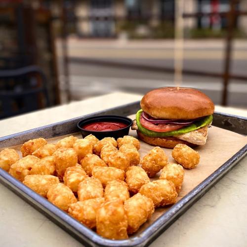 A tray with a sandwich topped with lettuce and tomato, alongside a serving of crispy tater tots and a small cup of ketchup.