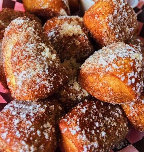 A close-up of golden-brown, sugar-dusted pastries piled in a pink basket.