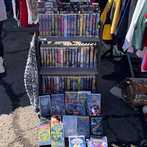 A display of VHS tapes on a shelf, featuring titles like E.T., Pokémon, and Batman, at a market.