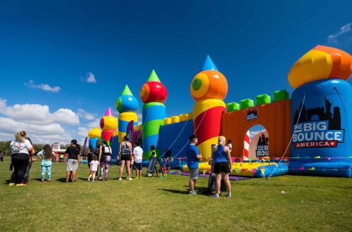 A colorful inflatable bounce house with people waiting in line on a sunny day.