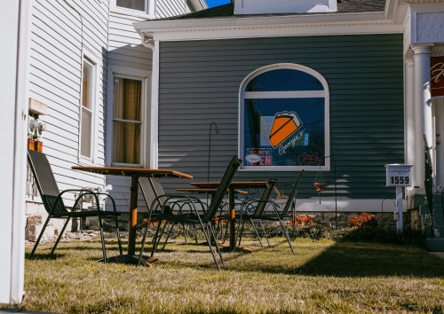 Outdoor seating area with tables and chairs in front of a building, featuring a window with an "Open" sign.