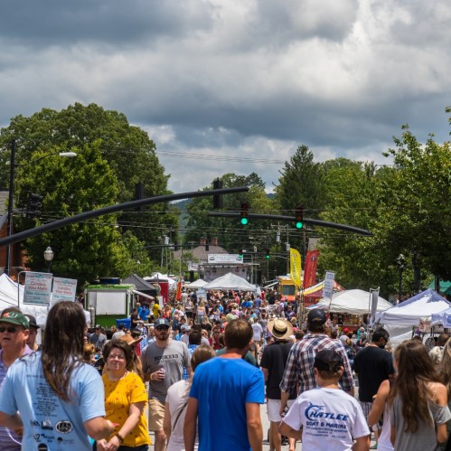 A bustling street fair with crowds, tents, and green traffic lights under a cloudy sky.