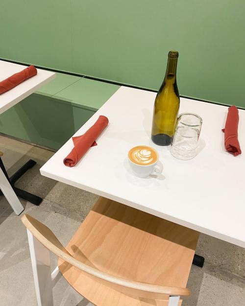 A minimalist café table with a latte art cup, a glass, a wine bottle, and neatly rolled napkins.