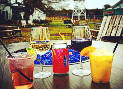 Four drinks on a table: a cocktail, a can, and two glasses of wine, with a vineyard backdrop and fire pit.