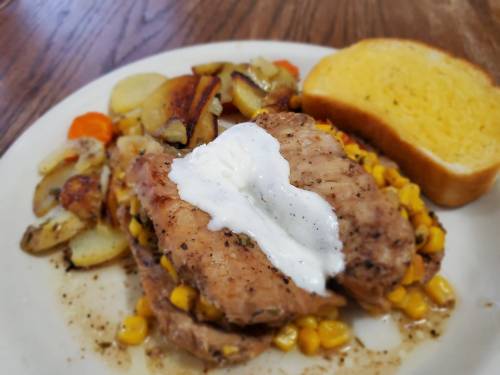 A plate of seasoned salmon topped with sour cream, served with roasted potatoes, carrots, and a slice of bread.
