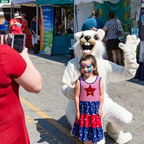 A girl in a star-patterned dress poses with a person in a polar bear costume at a festive outdoor event.