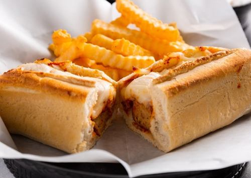 A close-up of a sandwich filled with meat and melted cheese, served with crinkle-cut fries on the side.