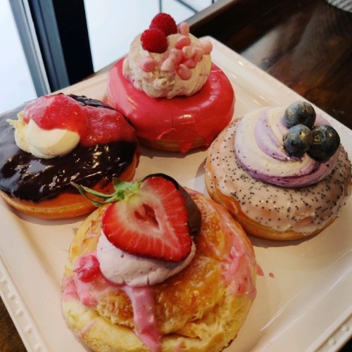 A plate of colorful donuts topped with various frostings, fruits, and whipped cream.