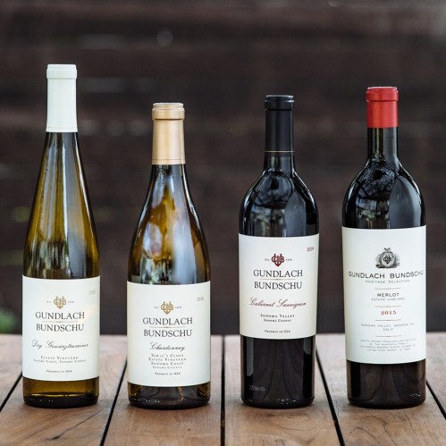 Four bottles of Gundlach Bundschu wine, including a Sauvignon Blanc, Chardonnay, and two red varieties, displayed on a wooden surface.