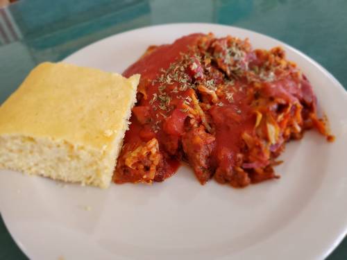 A plate of enchiladas topped with red sauce and herbs, served with a side of cornbread.