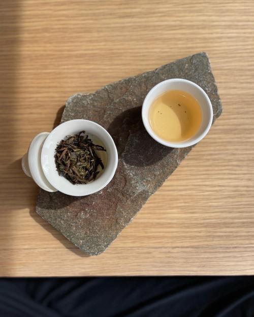 A stone slab holds a cup of brewed tea and a bowl of loose tea leaves, set against a wooden surface.