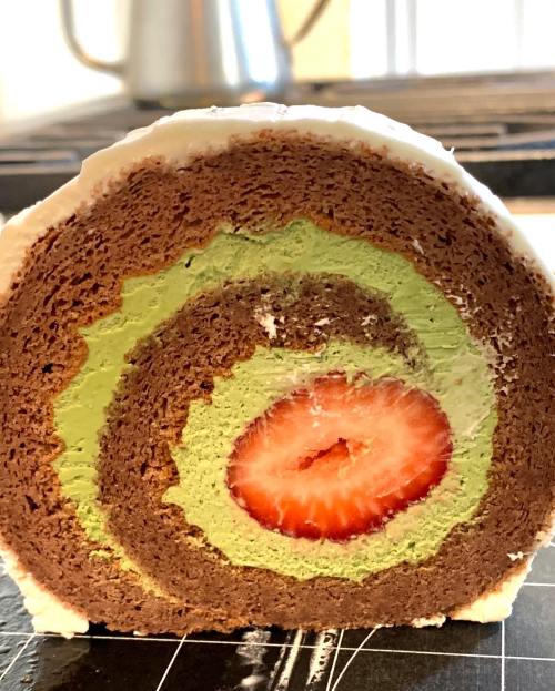 A cross-section of a colorful cake roll featuring chocolate, green layers, and a strawberry in the center.
