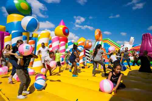 A vibrant inflatable playground filled with children playing with beach balls under a blue sky.