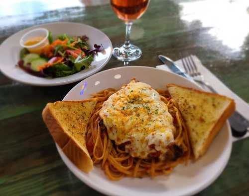 A plate of spaghetti topped with melted cheese, served with garlic bread and a side salad, alongside a glass of drink.