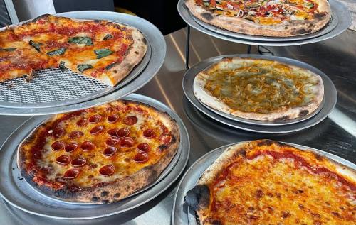 A display of six pizzas on metal trays, featuring various toppings like pepperoni, vegetables, and cheese.