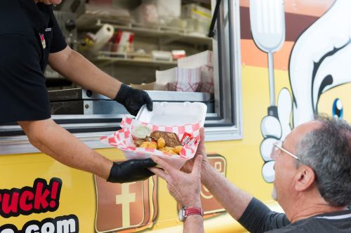 A food truck employee hands a takeout container to a customer at the window.