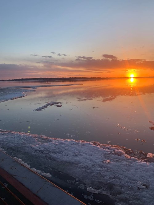 A serene sunset over a frozen lake, with ice fragments floating and colorful clouds reflecting on the water's surface.