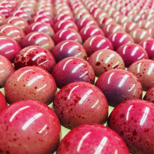 A close-up of numerous glossy pink spheres arranged in a grid pattern, showcasing various shades and speckled designs.