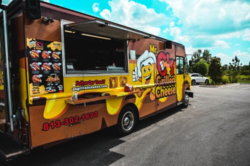 A colorful food truck named "Mr. C's Grilled Cheese" parked in a sunny area, featuring a variety of grilled cheese options.