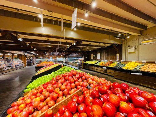 A vibrant grocery store aisle filled with colorful fruits, including red apples, green apples, and various other produce.