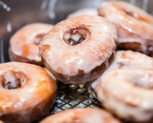 A close-up of glazed donuts stacked in a basket, showcasing their shiny, sweet icing.