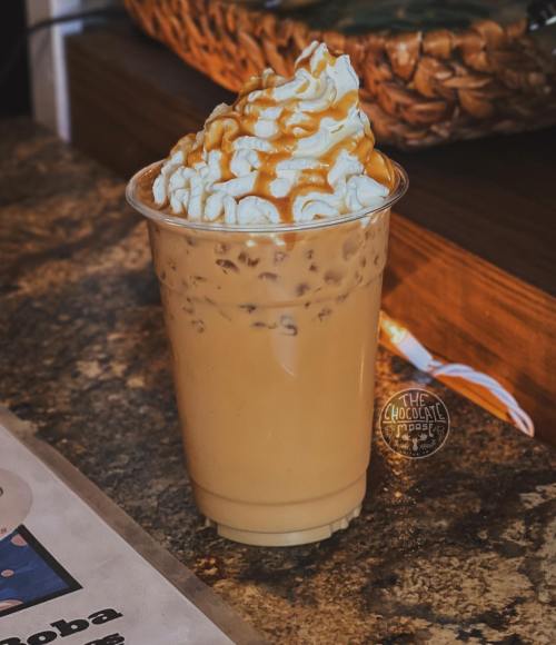 A clear cup filled with iced coffee topped with whipped cream and drizzled with caramel sauce on a wooden table.
